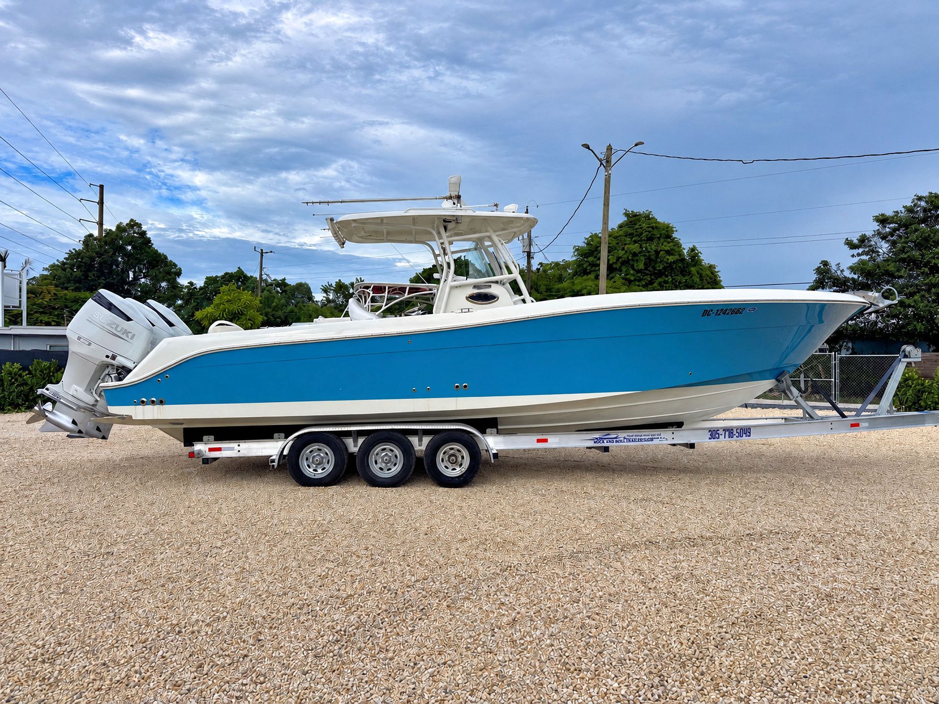 Blue-and-white center console boat on a trailer in a gravel lot under a clear sky