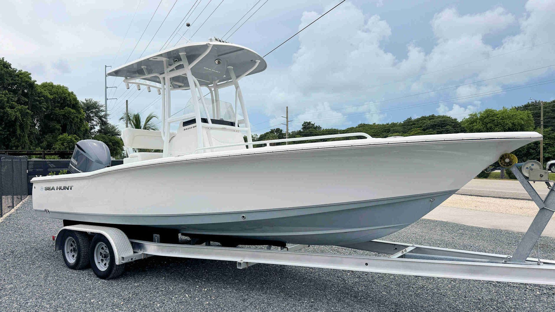 White center-console boat on a trailer in a gravel lot under a cloudy sky