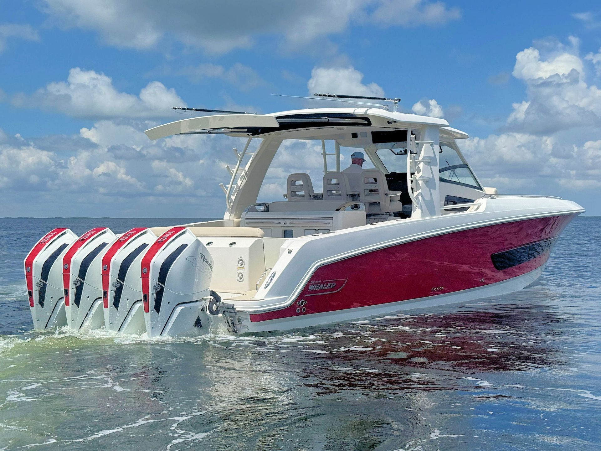 Red-and-white center console boat cruising on calm blue water under a partly cloudy sky.