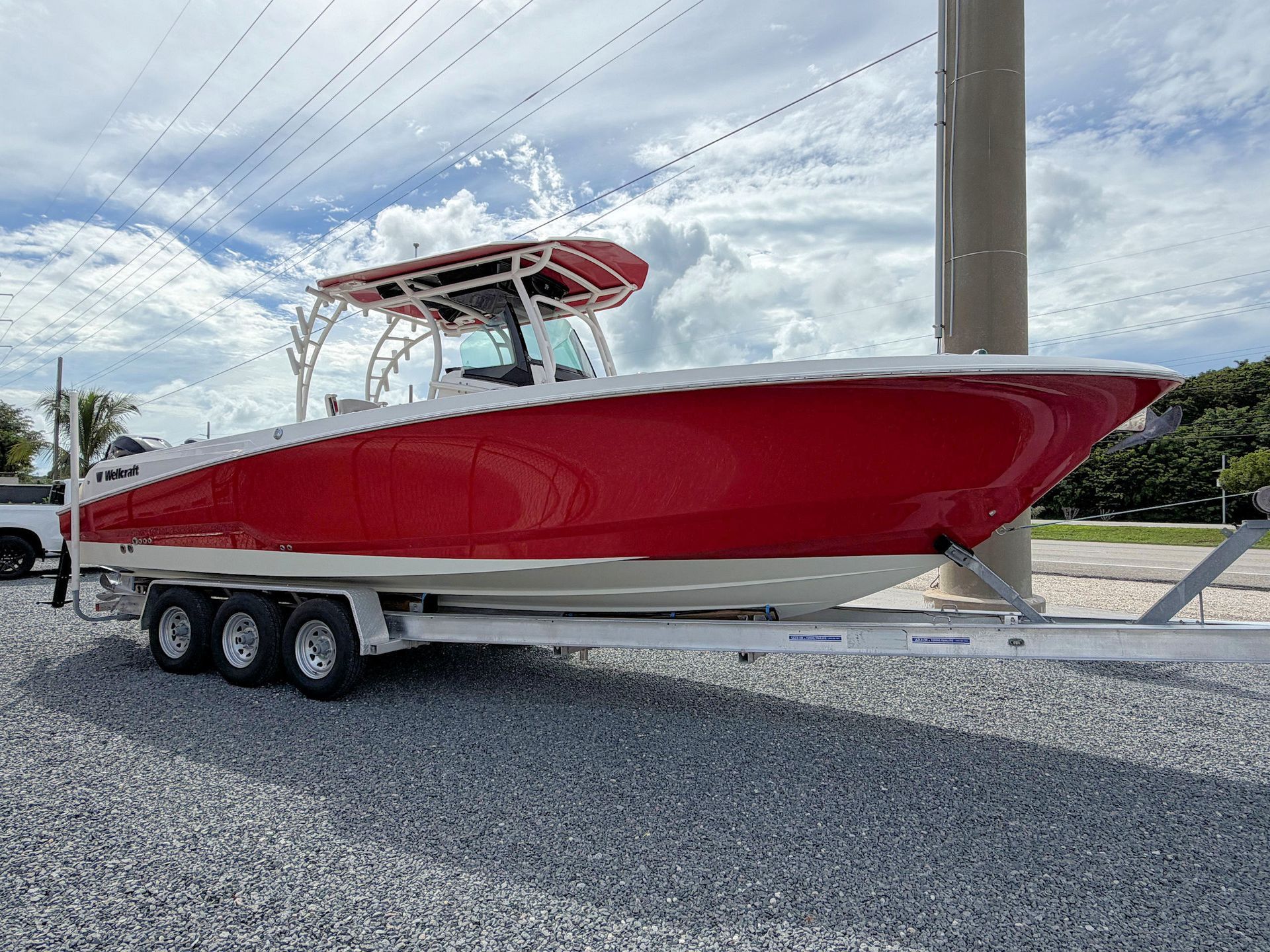 Red center-console fishing boat on a trailer beside a road under a cloudy sky