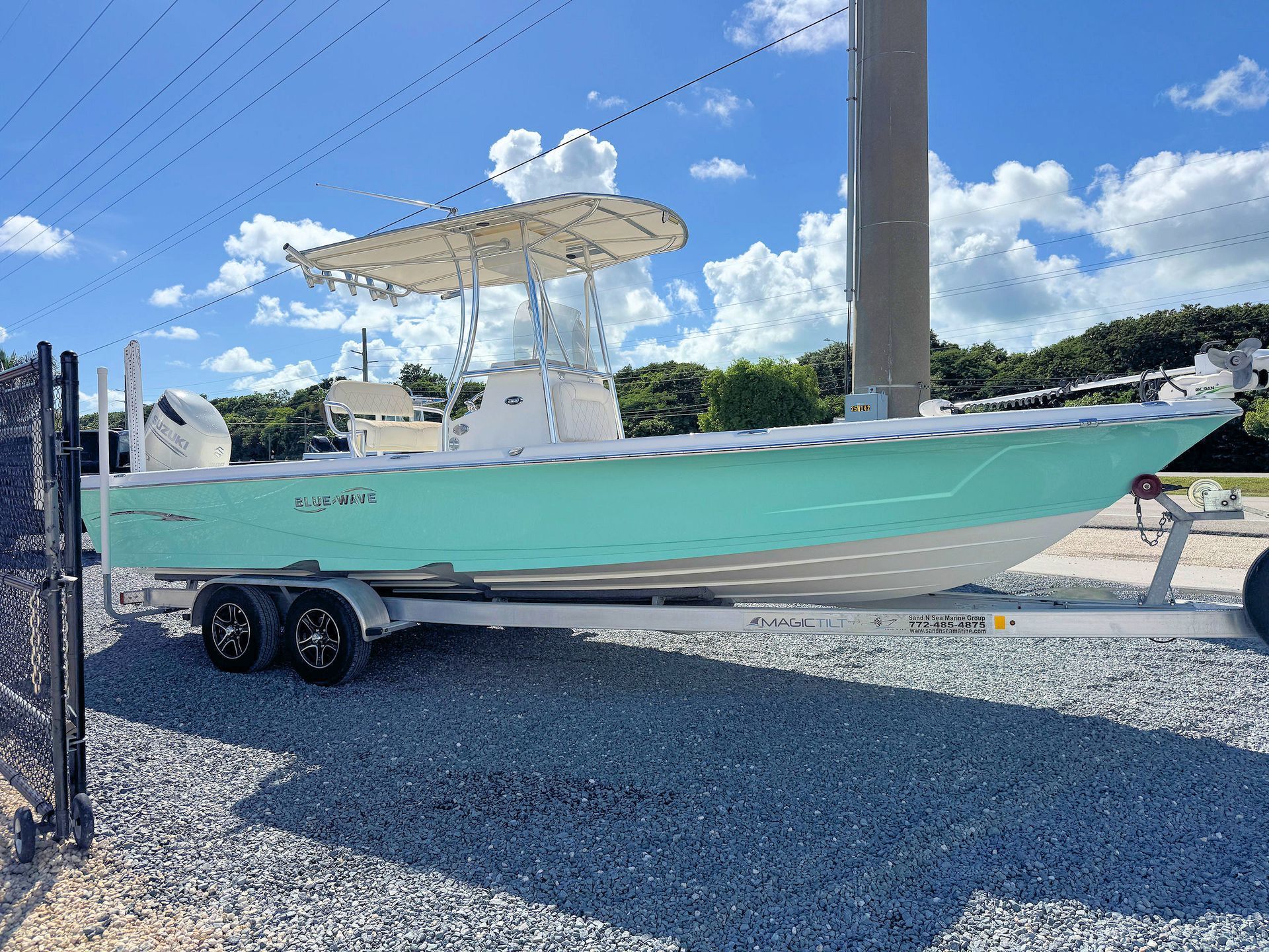 Mint green center-console bay boat on a trailer in a gravel lot under a partly cloudy sky