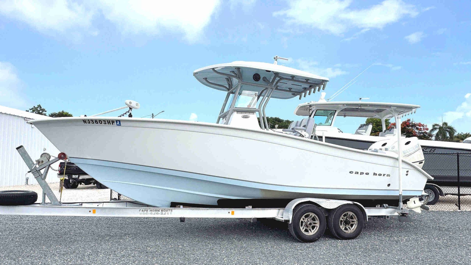 White center-console fishing boat on a trailer parked on gravel under a blue sky