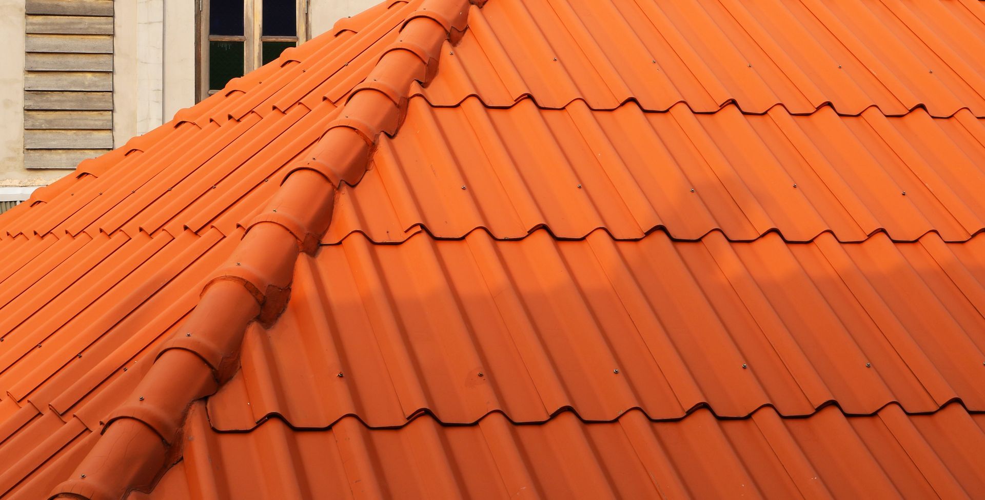 Orange terracotta roof tiles on a house, with a sloped ridge and brick chimney
