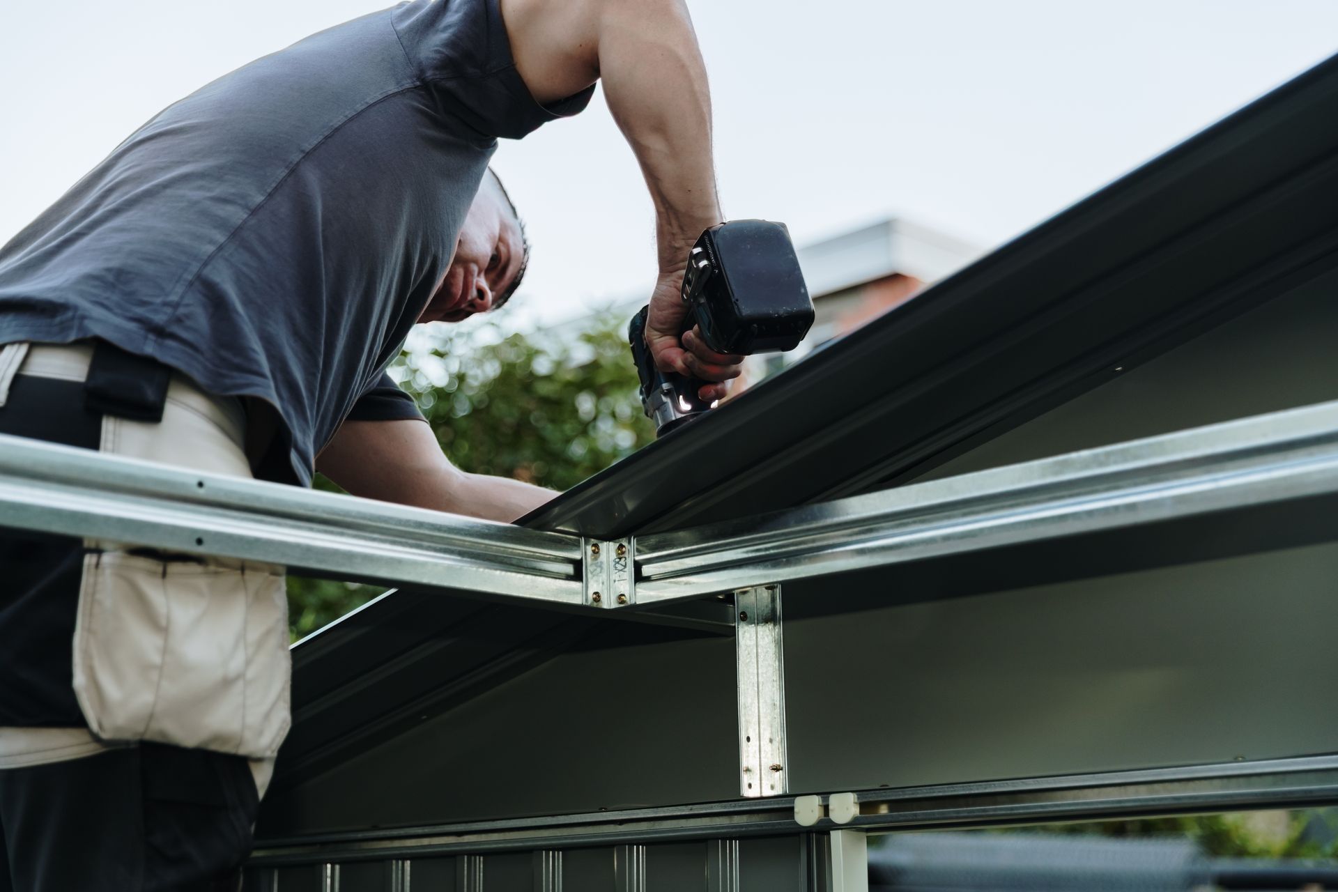 Worker using a drill to install a metal roof panel on a building exterior