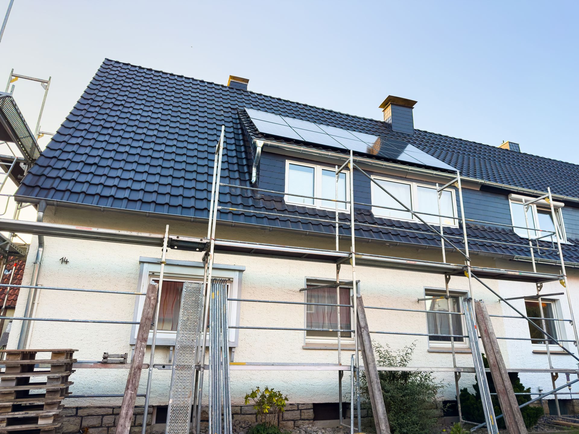 House under renovation with scaffolding and ladders, dark blue roof, and white exterior walls.