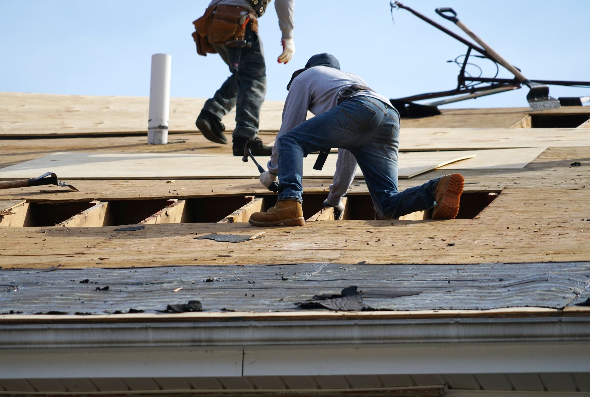 Roofers repairing a damaged roof with plywood and tools under a clear sky