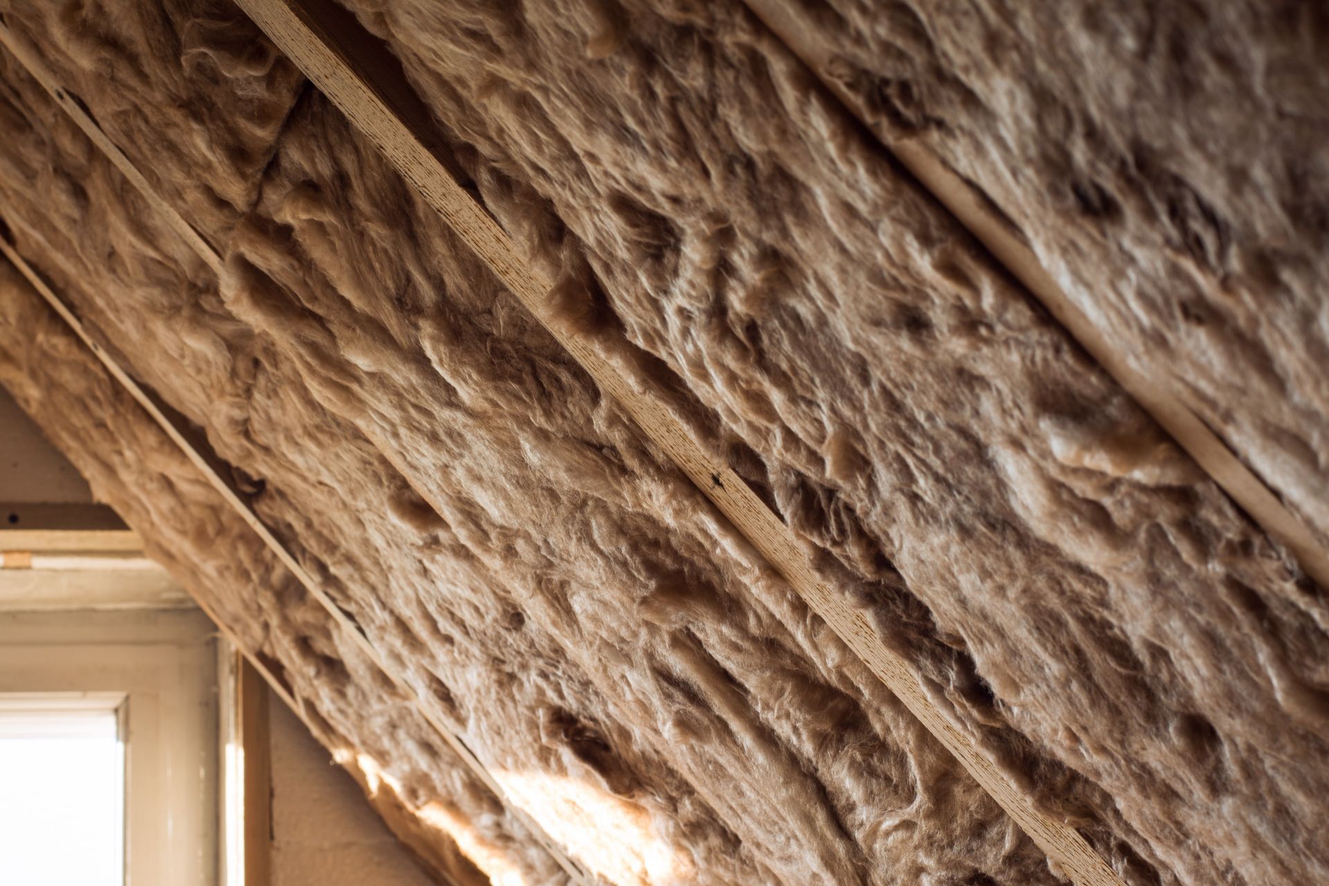 Close-up of exposed attic insulation sloping beside a window frame.