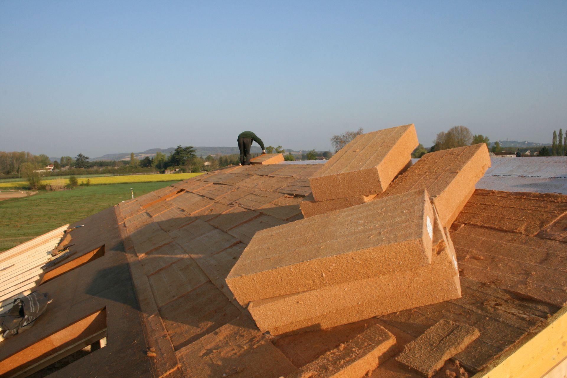 Piles of orange bricks and debris on a rooftop under a clear sky, with fields in the distance