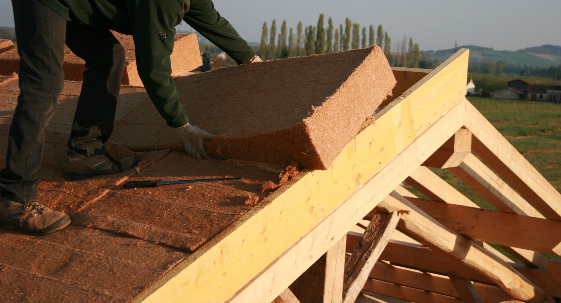 Worker placing roofing shingles on a sloped roof at a construction site