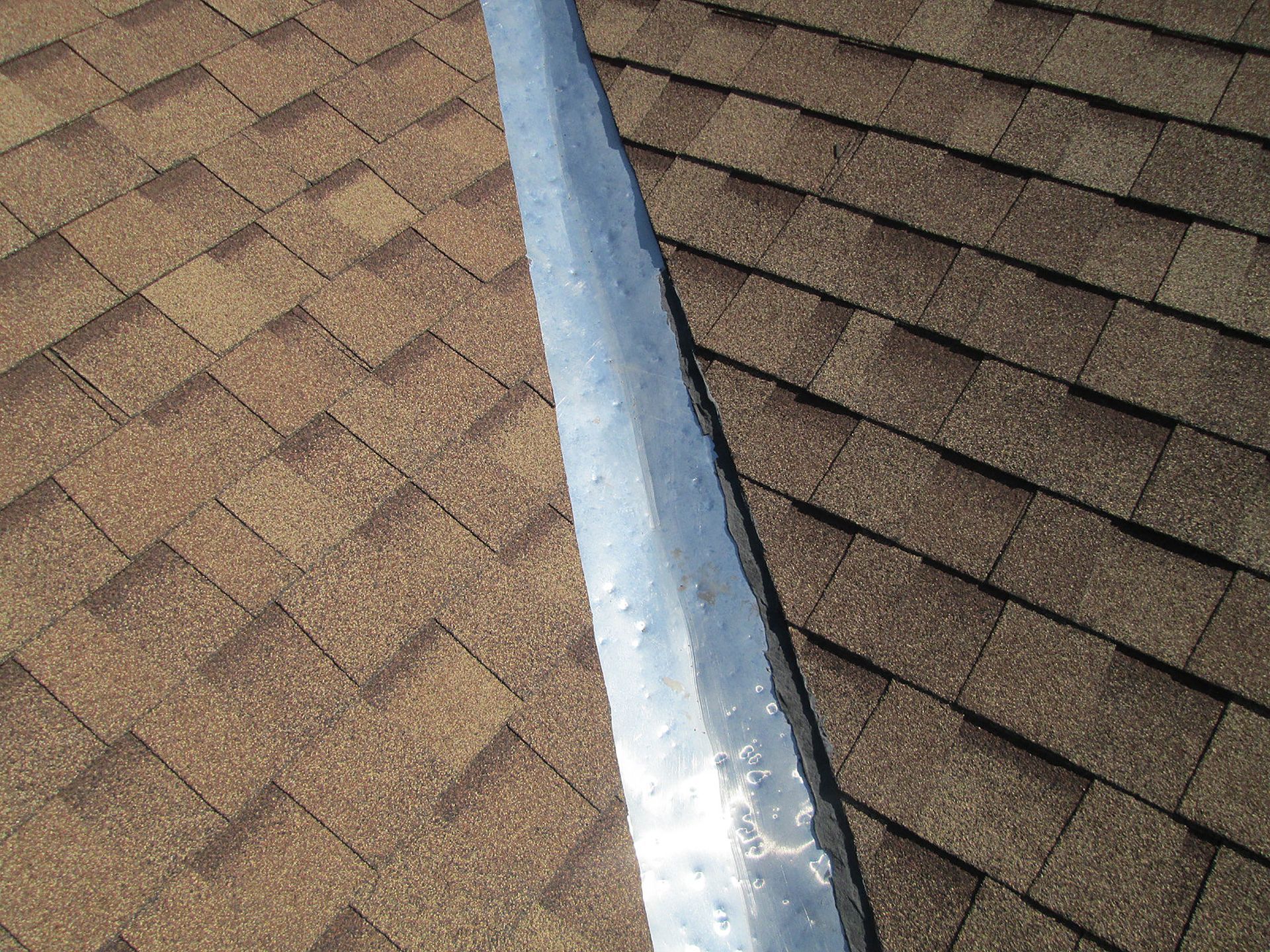 Rooftop shingles with a shiny metal roof vent flashing running vertically through the center.