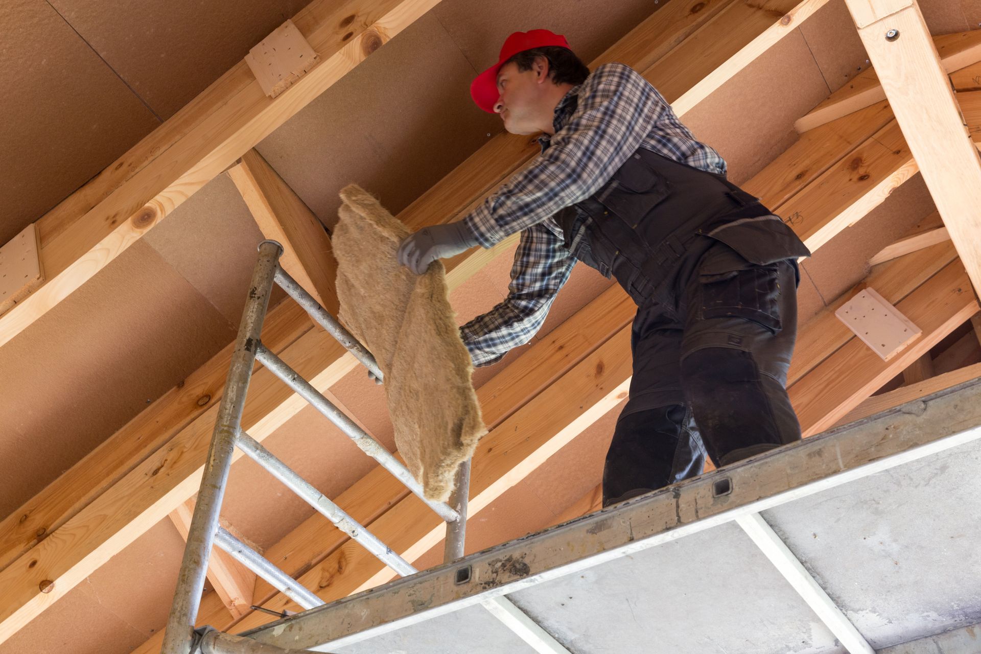 Worker on a ladder installing insulation in an unfinished attic ceiling