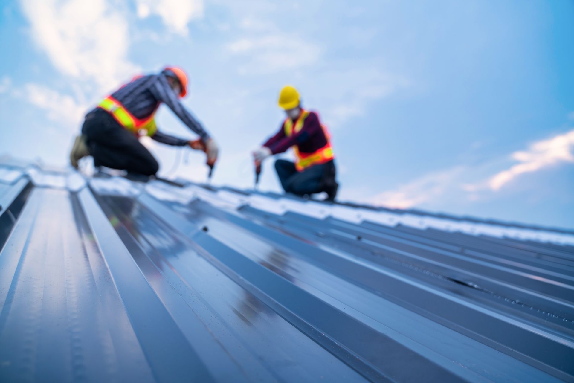 Two workers in hard hats installing a metal roof under a blue sky
