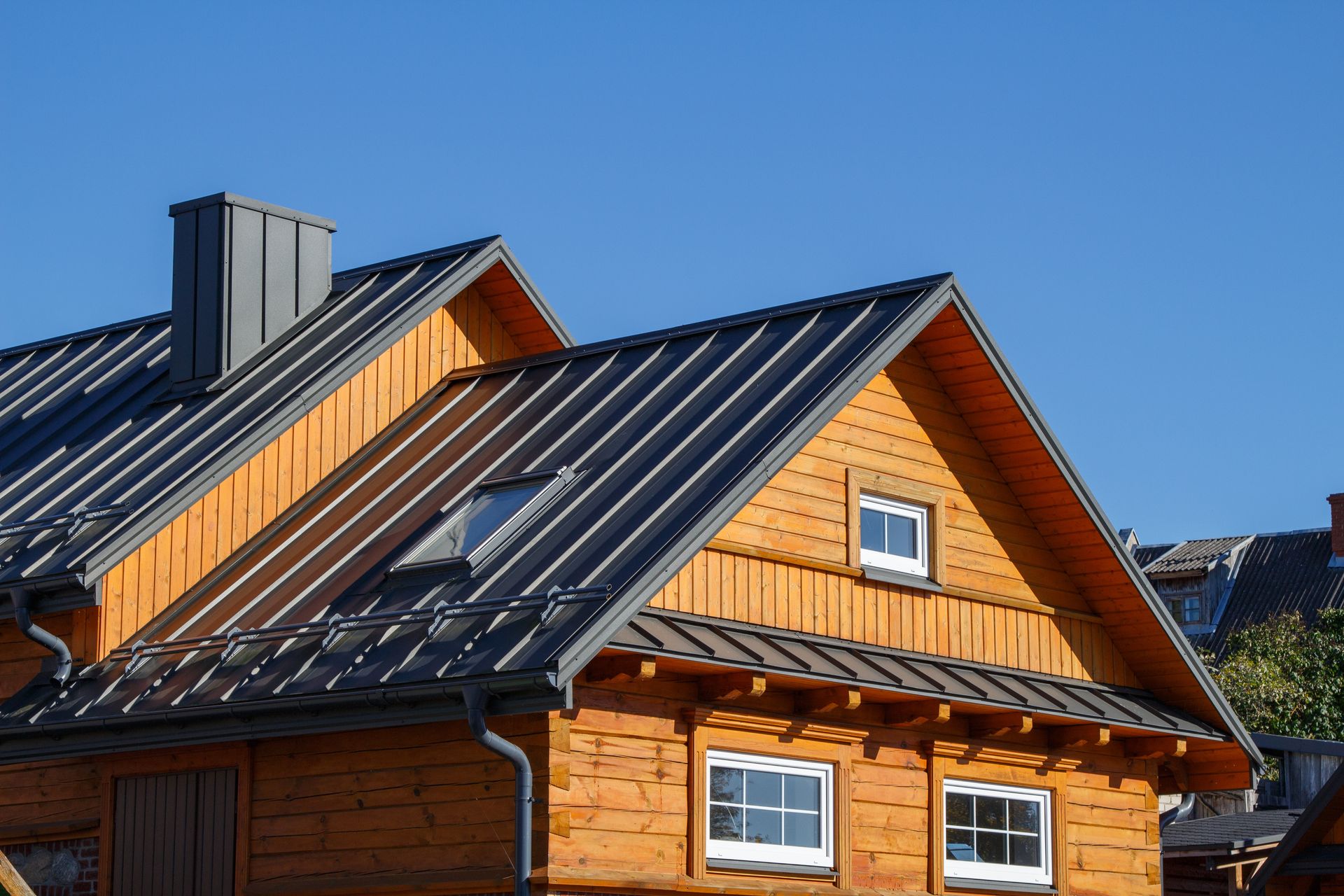 Two wooden houses with dark metal roofs and solar panels under a clear blue sky.
