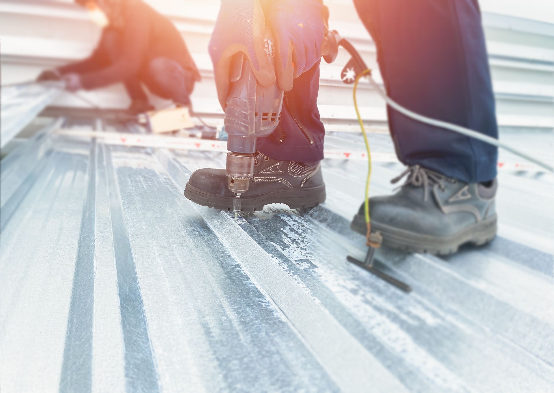 Workers installing roofing with power tools on a sunlit metal roof