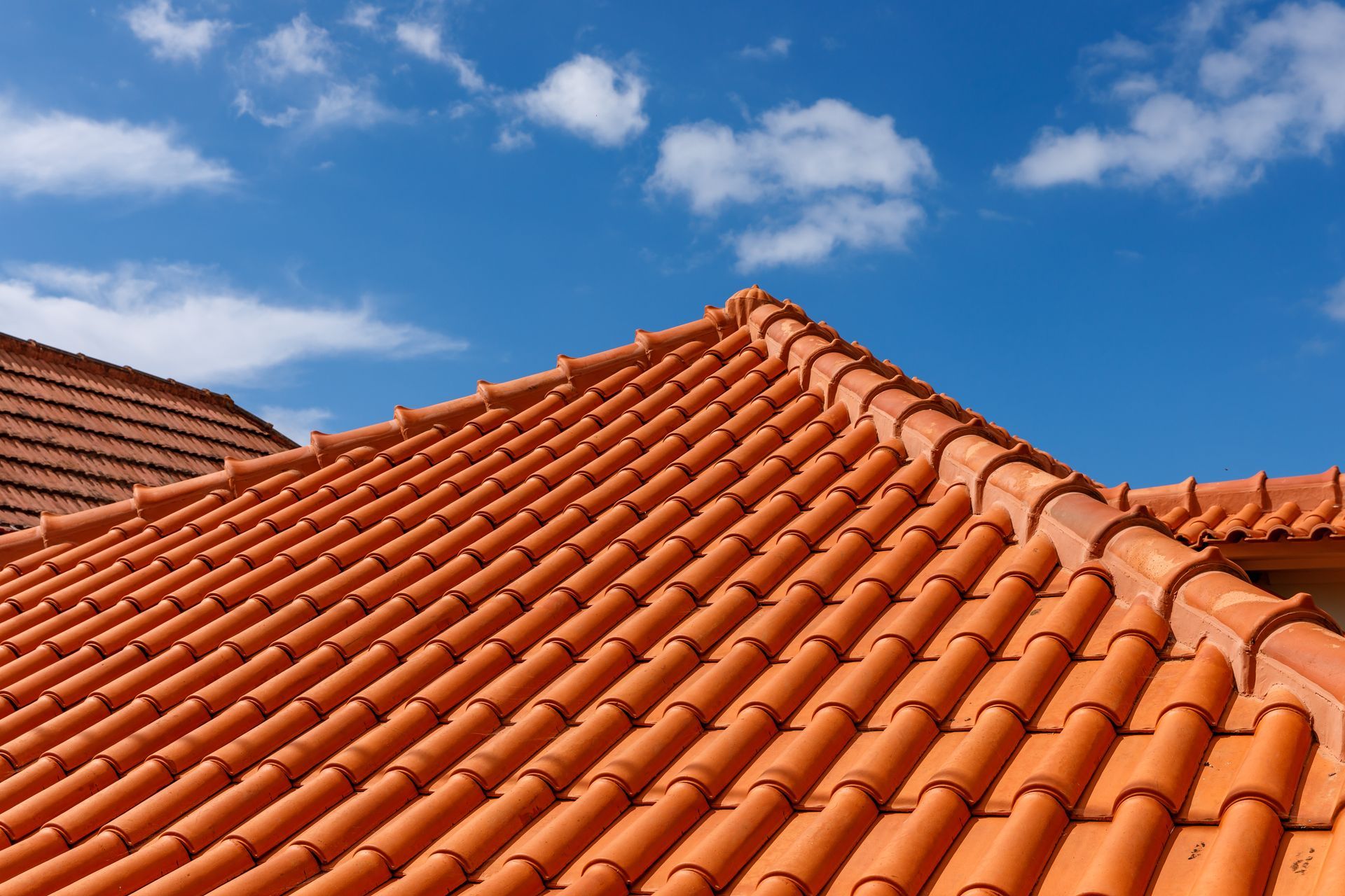 Red terracotta tiled roof under a blue sky with clouds