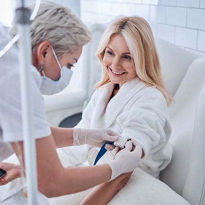 Woman receiving IV treatment in medical setting; nurse prepares arm.