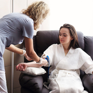 Person receiving intravenous fluids. Medical staff, gloved hands; arm on pillow with IV line and bandage.