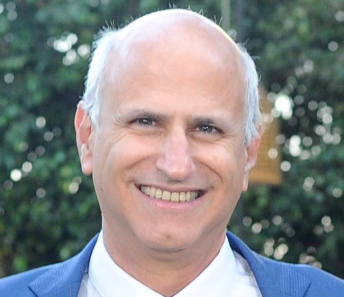 A photo of Udi in a suit and tie smiling for the camera.