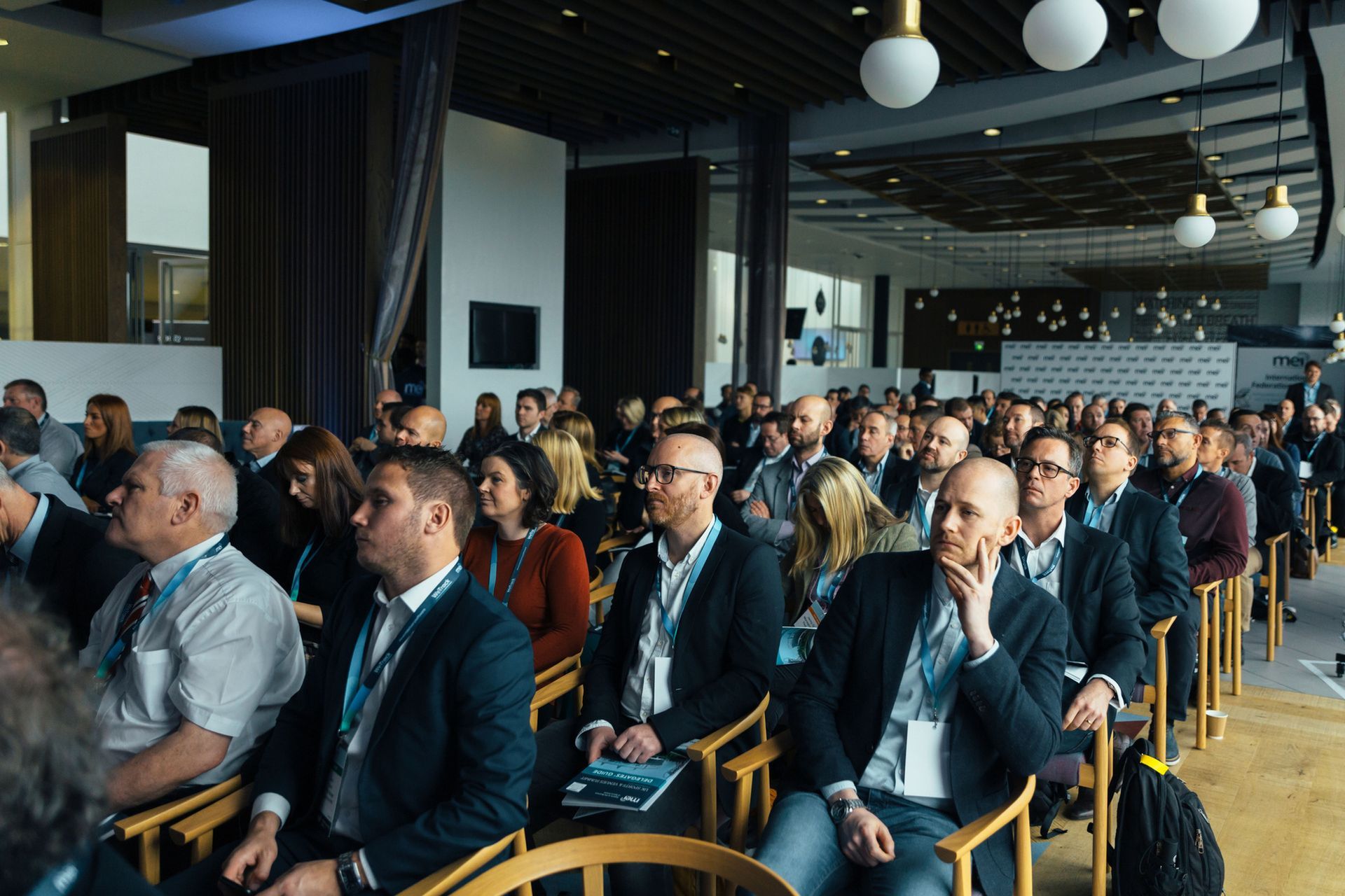 Audience seated in a modern conference room, listening attentively during a presentation.