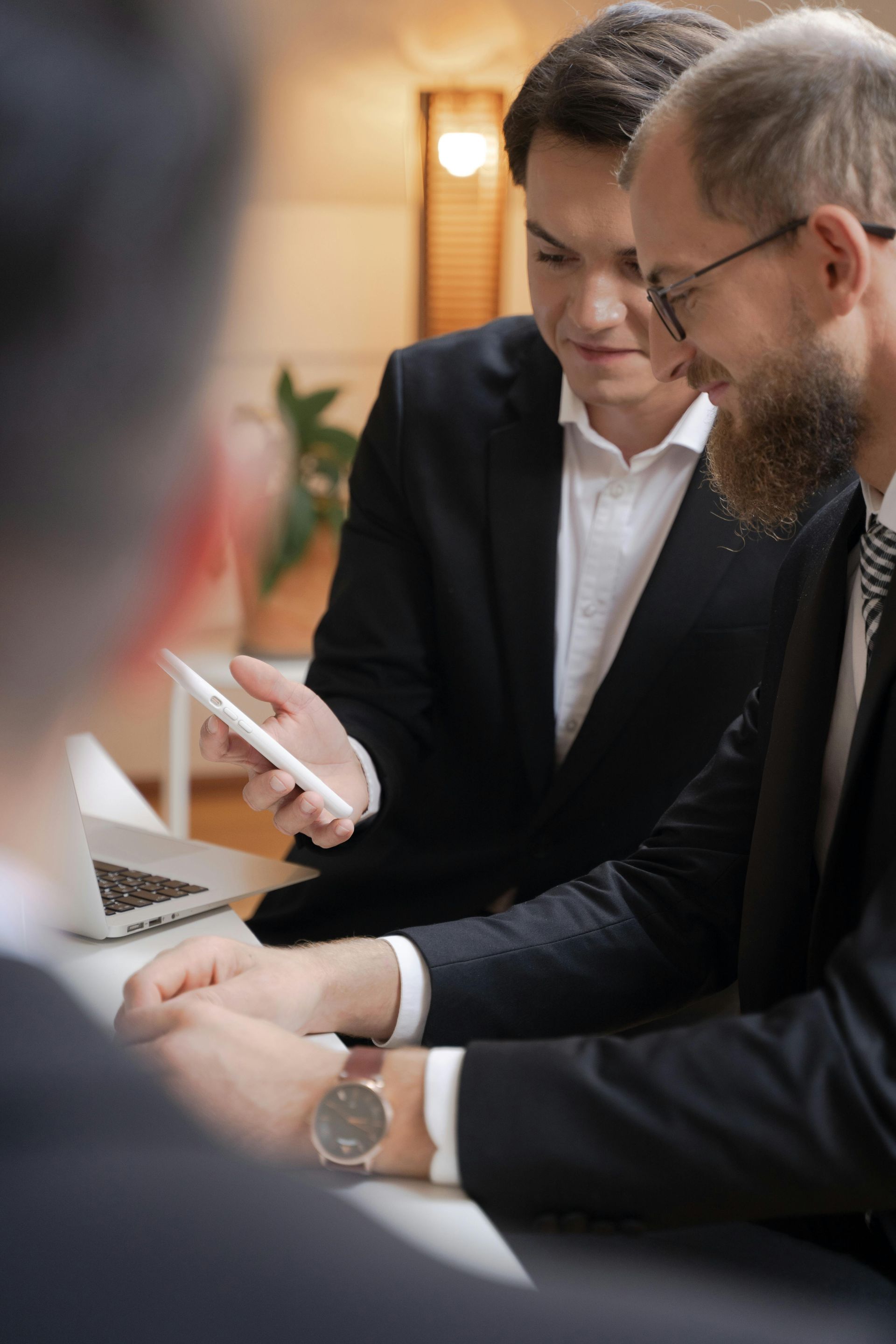 A group of men are sitting at a table looking at a tablet.
