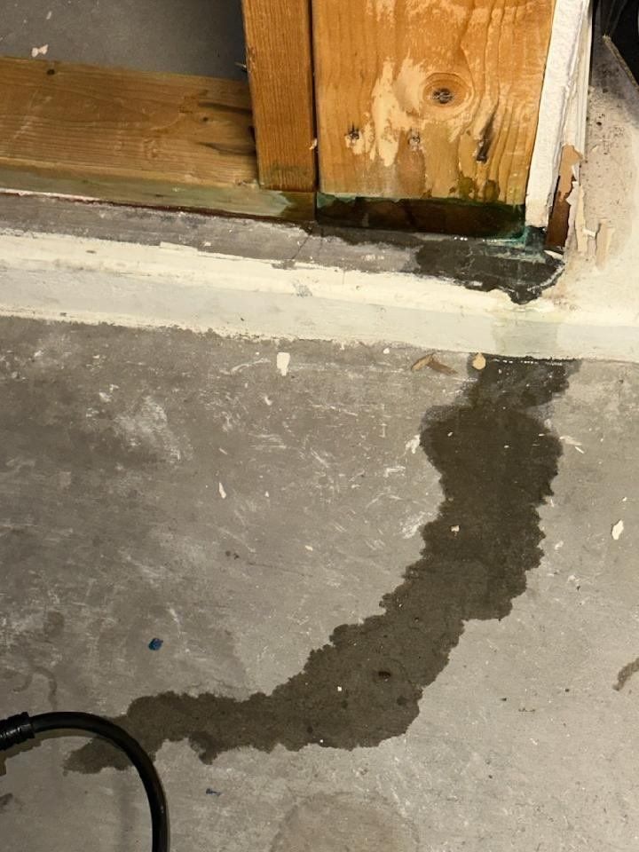 A puddle of water on the floor next to a wooden wall.