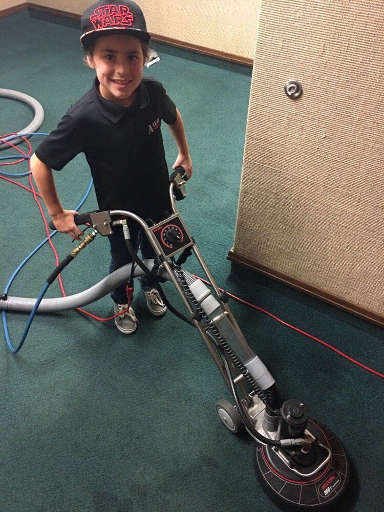 A young boy is standing next to a vacuum cleaner on a green carpet.