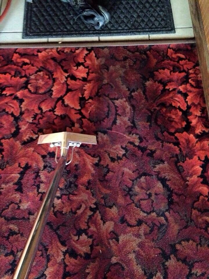 A red rug is being cleaned with a vacuum cleaner.
