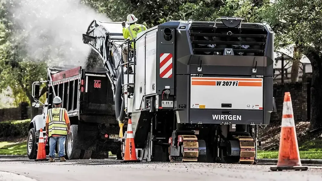 Road construction crew with two paving machines, workers, and orange cones on a smoky street