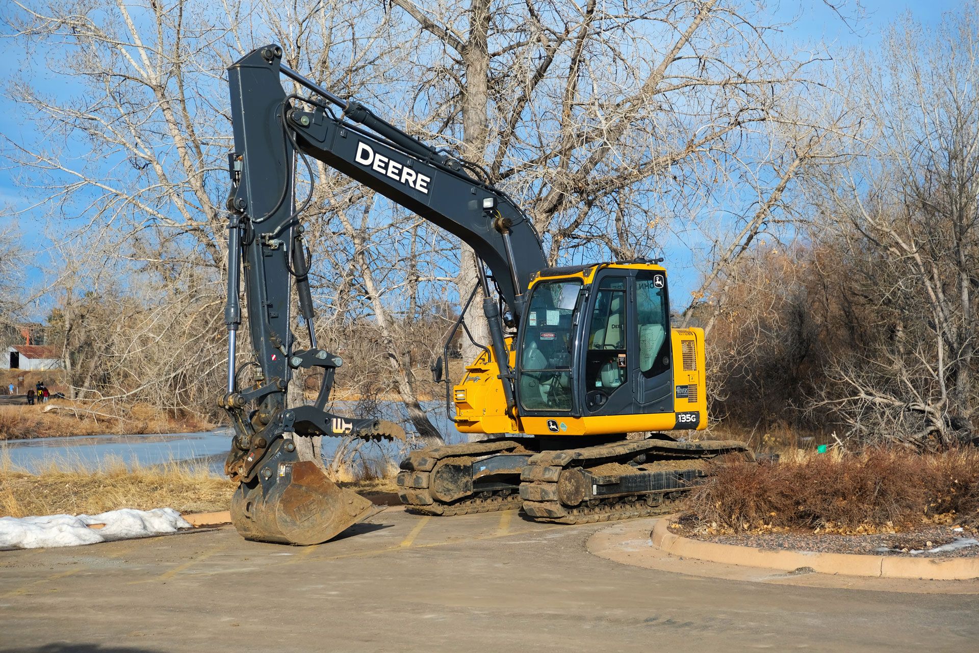 Yellow backhoe clearing overgrown brush in a field