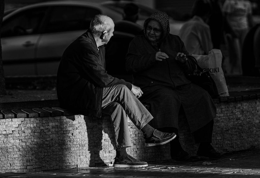 Two people sit on a stone bench at night, one in a dark coat and the other wrapped in a blanket.