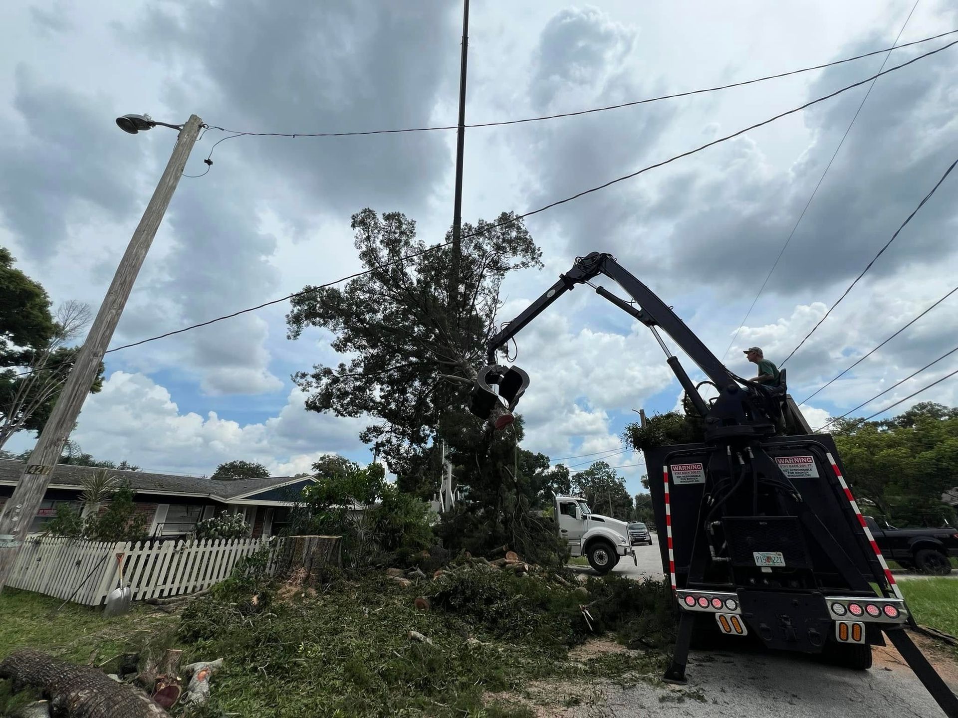 A crane is cutting down a tree in front of a house.