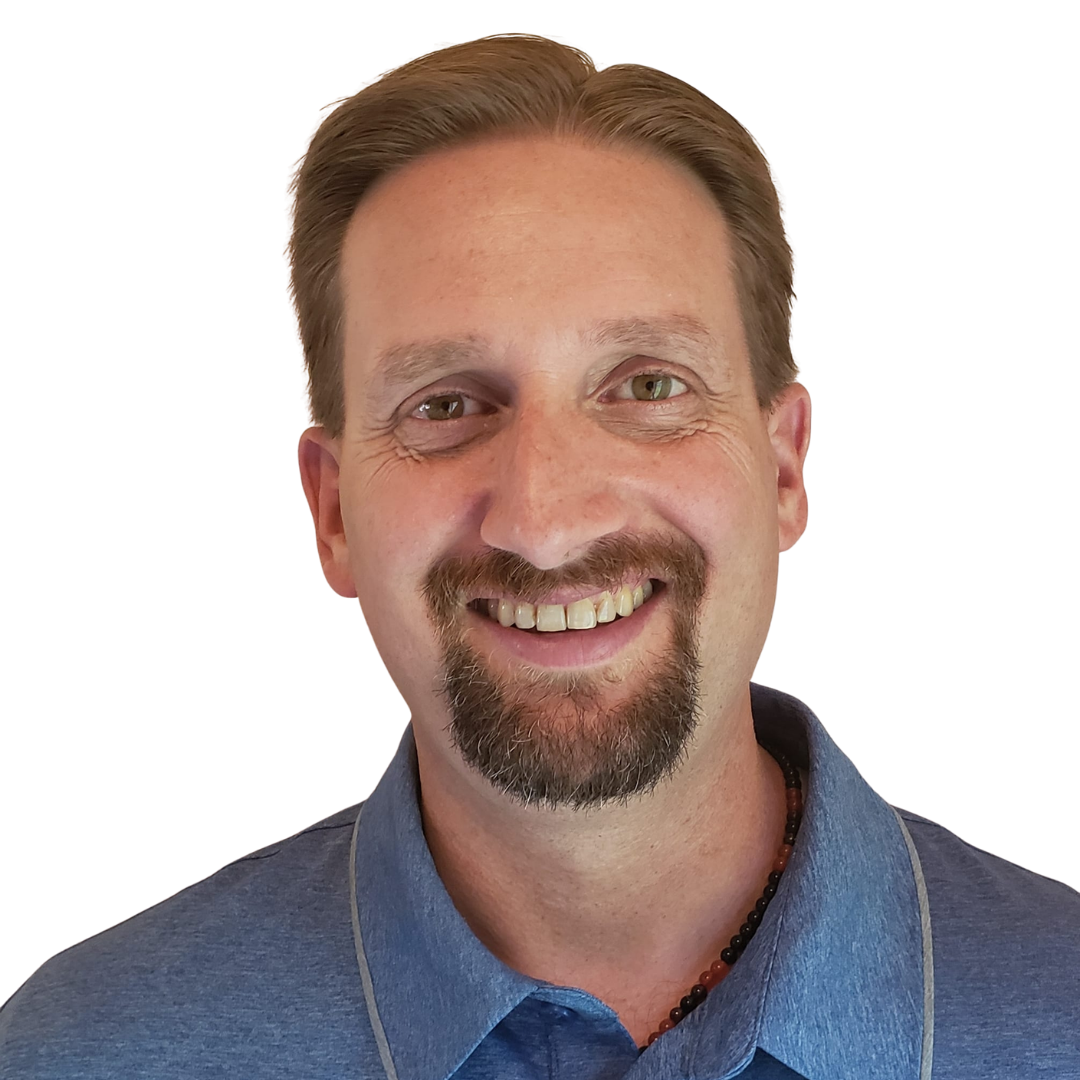 Smiling man with short brown hair and goatee wearing a blue collared shirt against a white background