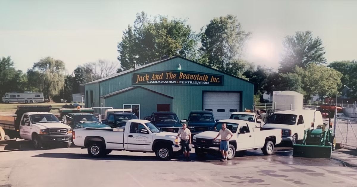 Classic car meet outside a green auto shop, with several vintage vehicles parked in front of the building.