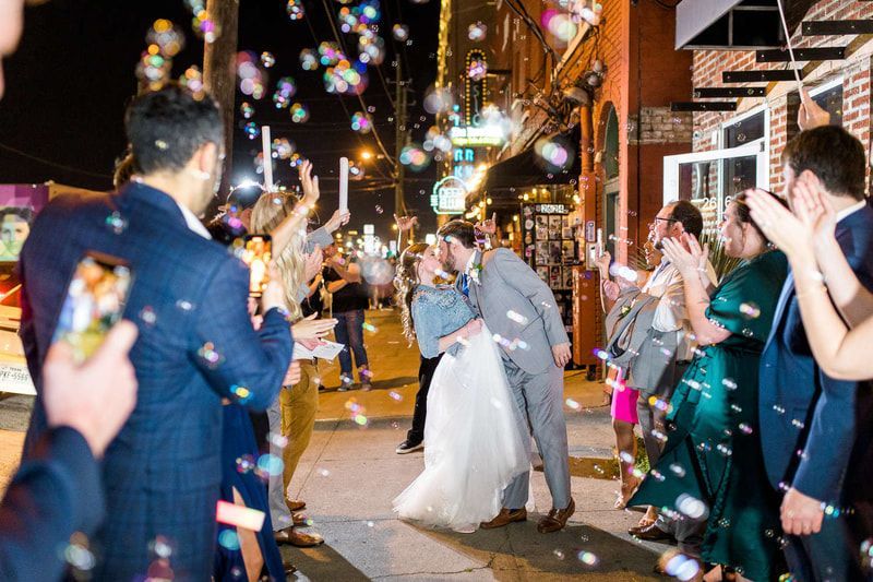 A bride and groom kissing in front of a crowd of people blowing soap bubbles.