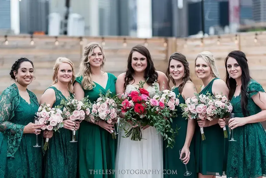 A bride and her bridesmaids in green dresses are posing for a picture.
