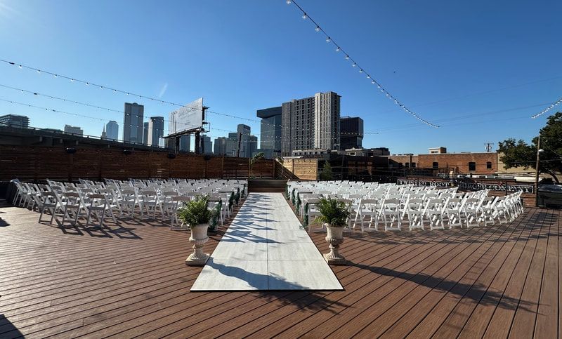 A wedding ceremony is taking place on a rooftop deck with a city skyline in the background.
