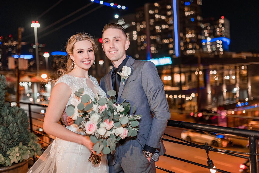 A bride and groom are posing for a picture in front of a city skyline at night.