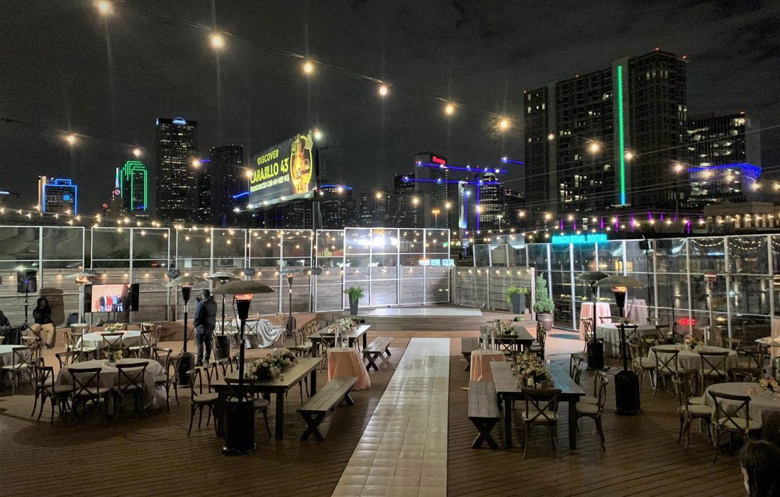 A large patio area with tables and chairs at night with a city skyline in the background.