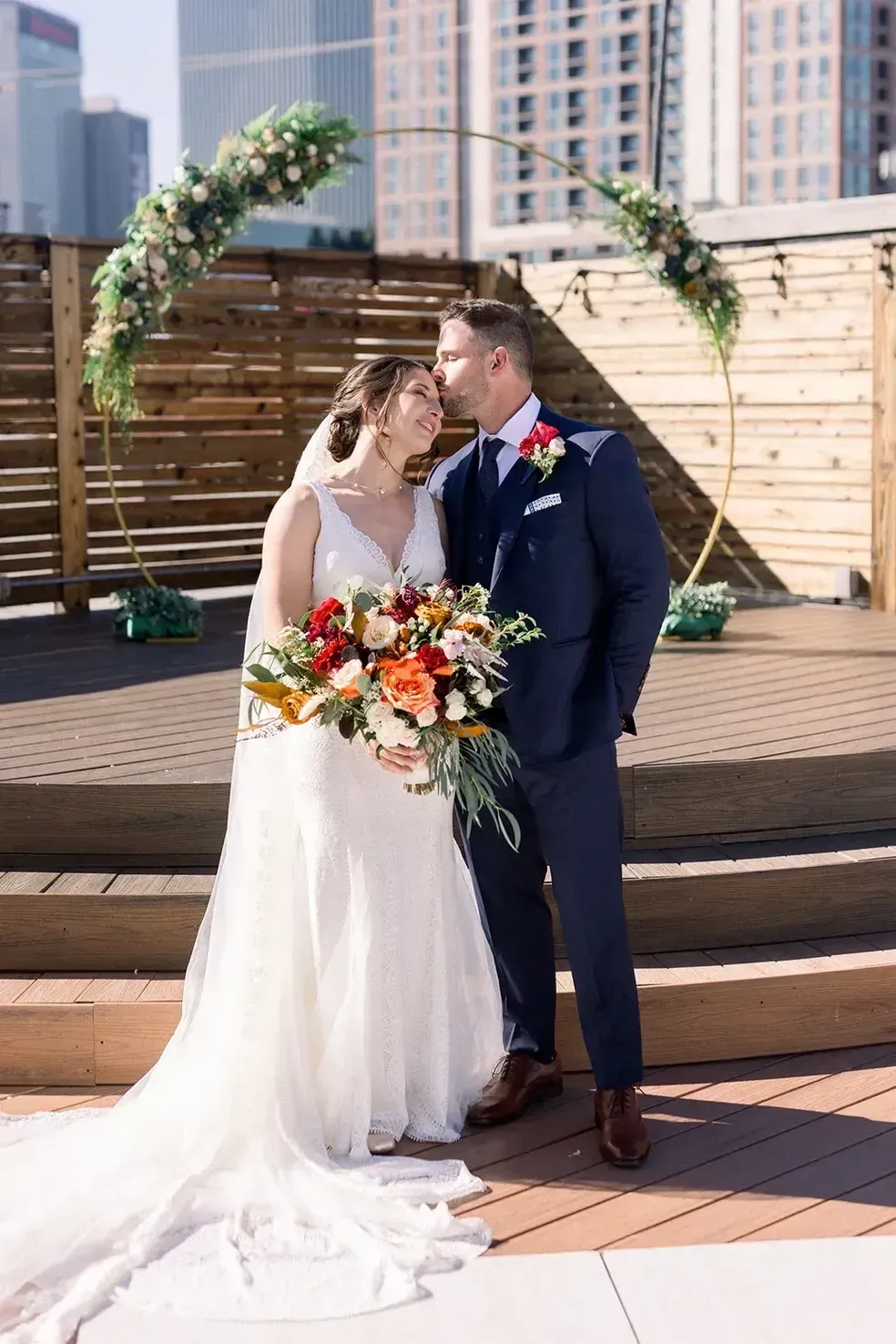 A bride and groom are kissing under a floral arch at their wedding.