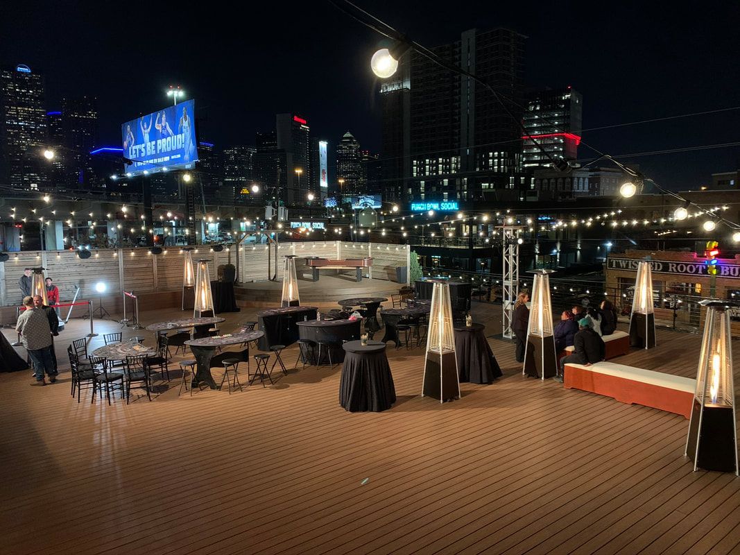 A large deck with tables and chairs and heaters at night.