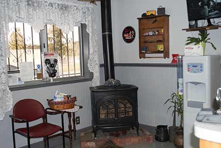 Cozy waiting room with wood stove, window, red chair, water dispenser, and small wooden cabinet. | Burrough & Sons Automotive Inc.