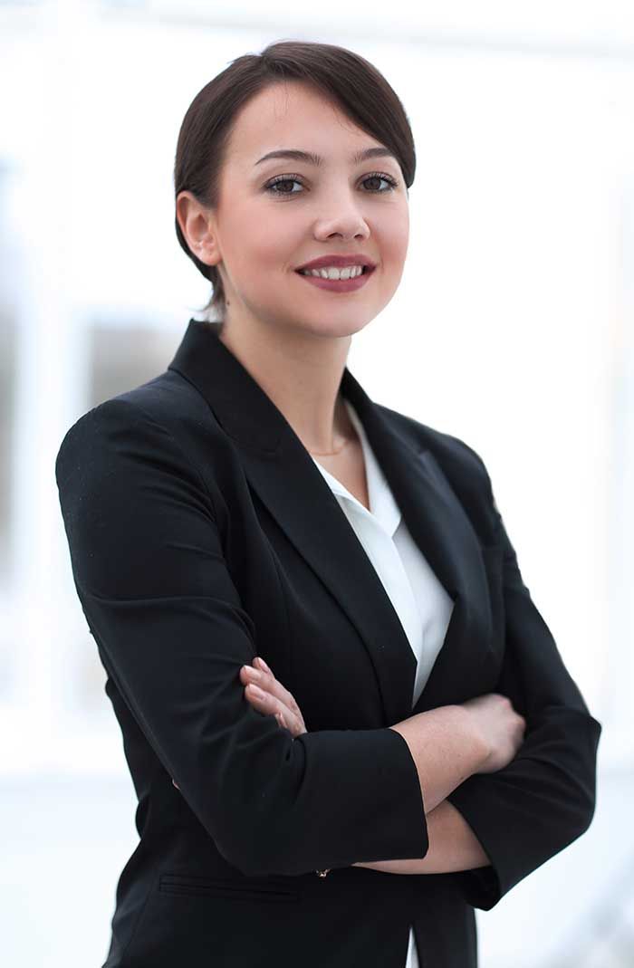 Woman in black blazer with arms crossed, smiling in a well-lit office.