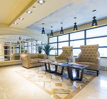 A bright, modern lobby with neutral armchairs, a sofa, a long dark coffee table, and pendant lighting under a blue ceiling.