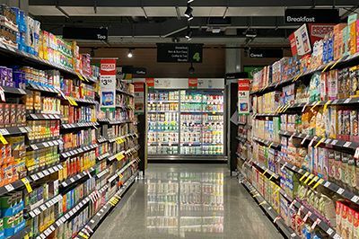 Grocery store aisle with shelves filled with packaged food products. Refrigerated section in the distance.