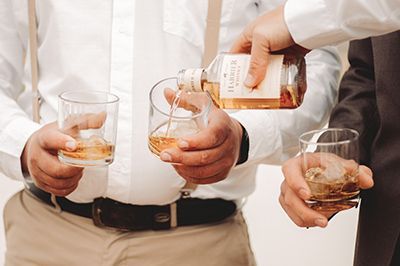 Man pouring whiskey into glasses, held by other men.