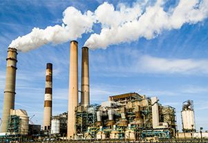Smokestacks releasing white smoke over an industrial power plant against a blue sky.