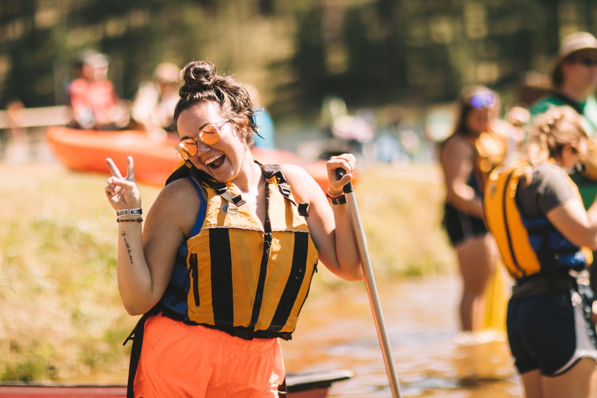 Person in orange and black outfit smiles and makes a peace sign at an outdoor event