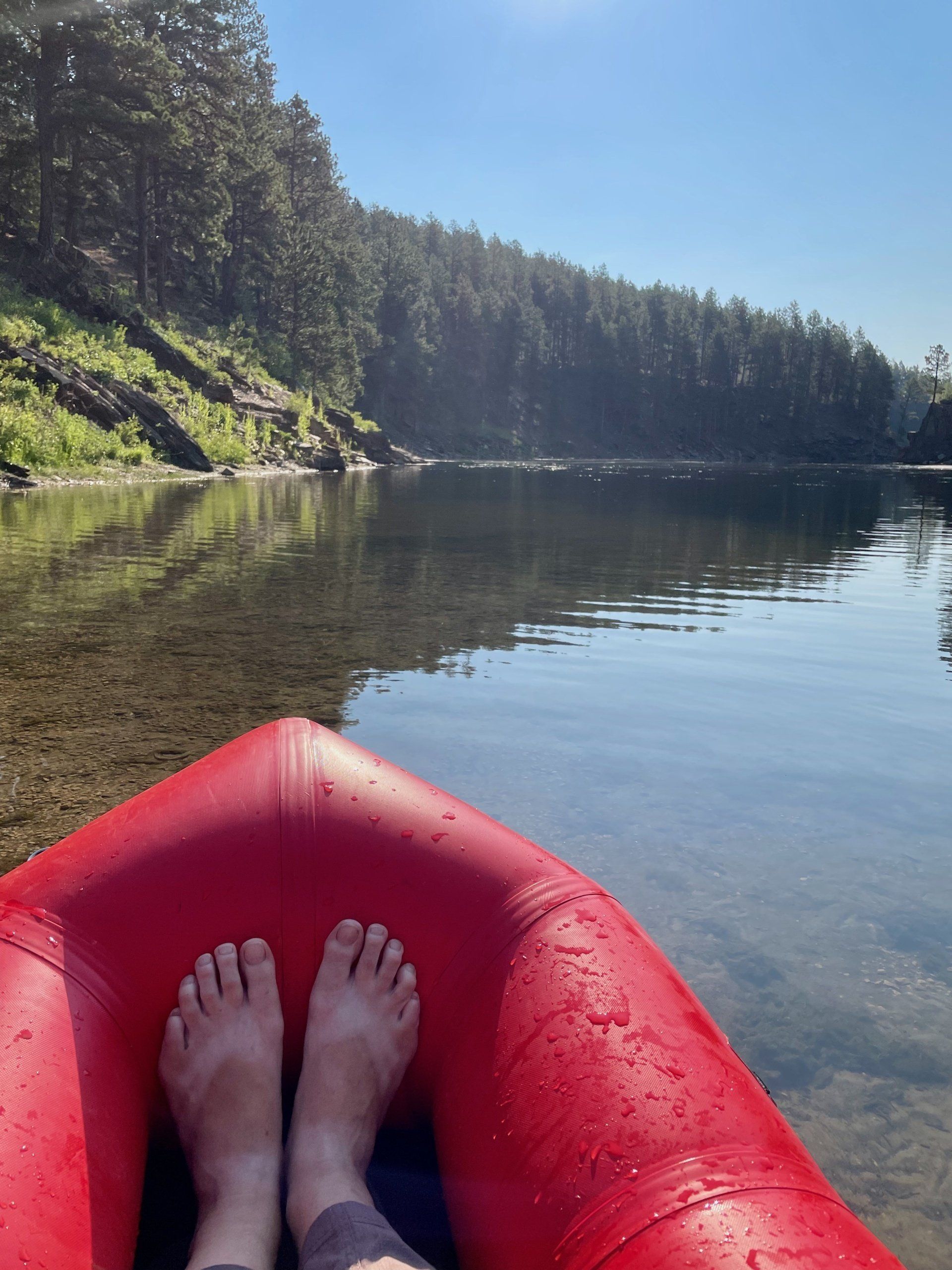 A person 's feet are resting on a red raft in the water.