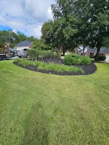 Green lawn and a landscaped bed with dark mulch, shrubs, and a tree. A truck is in the background.
