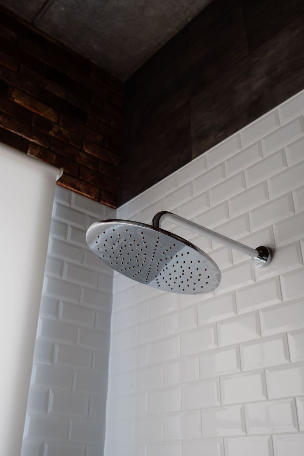 Modern round rain showerhead against white tile and dark wood ceiling